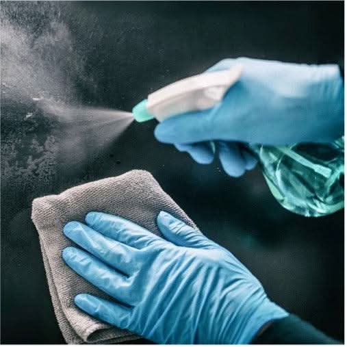 Person wearing blue gloves cleaning a surface with a cloth and spray bottle.