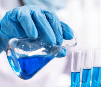 Person in blue gloves transferring blue liquid from a beaker into test tubes.