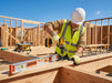 Worker in a construction site using tools on wooden beams. Wearing Tuff Gard Kevlar Shell NBR‑Palm Coated Glove – Yellow & Black