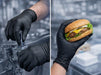 Gloved hands working on machinery and holding a burger with a blurred cityscape background.