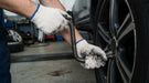 Person changing a tire with tools in a garage setting while wearing Tuff Gard Cotton/Polyester Knit Glove