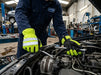Mechanic working on a car engine in a garage wearing high-visibility gloves.