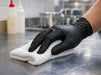 Person cleaning a surface with a white cloth and black gloves in a kitchen setting