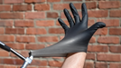 Person putting on black nitrile glove against a brick wall background