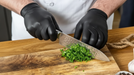 Chef wearing black nitrile gloves chopping fresh herbs on a wooden cutting board